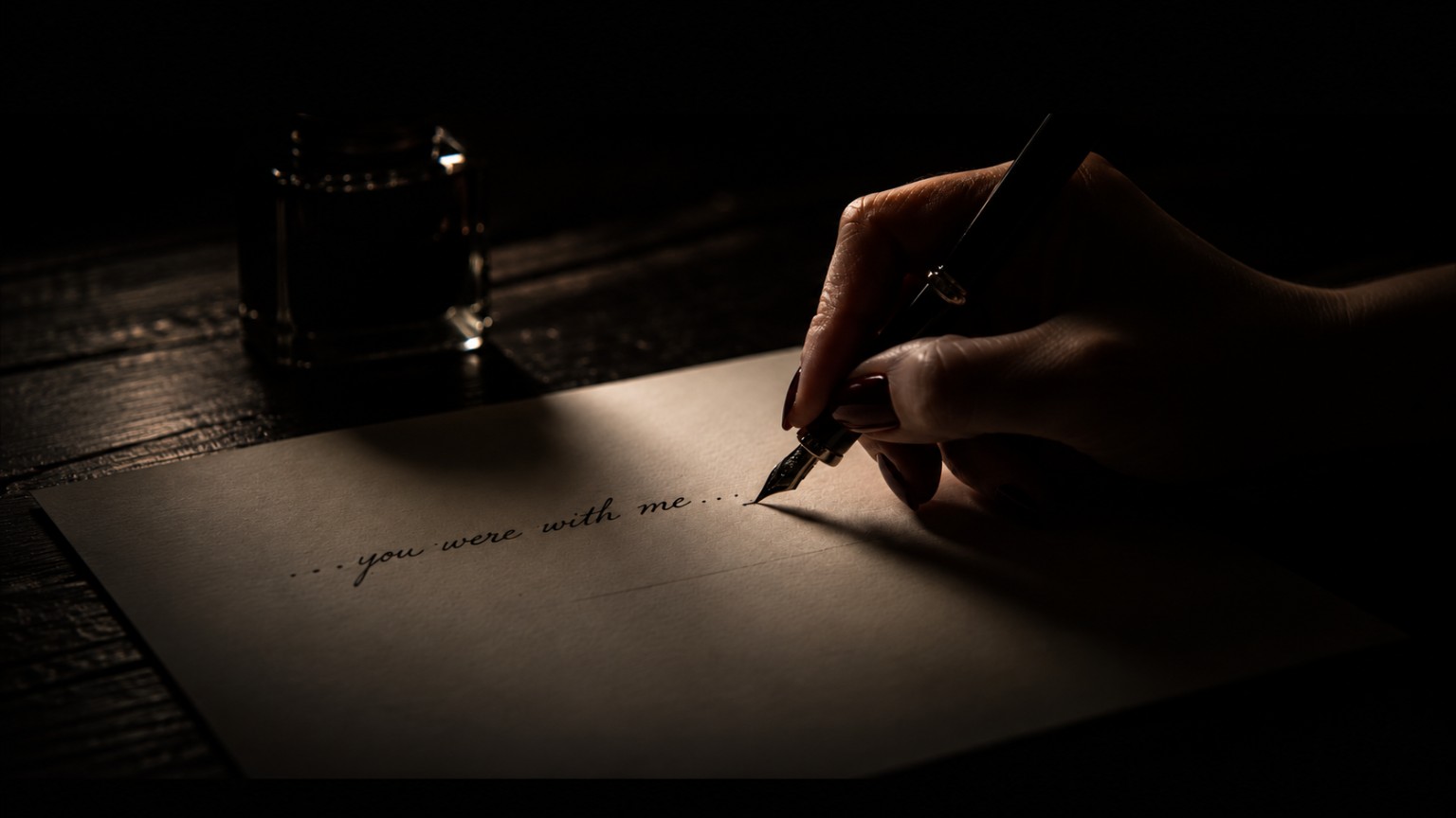 A hand writing 'you were with me' in ink by lamplight