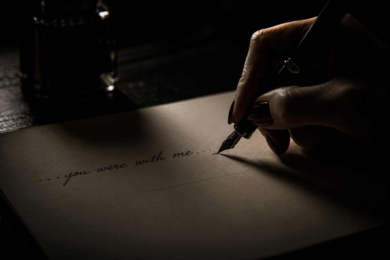 A hand writing 'you were with me' in ink by lamplight